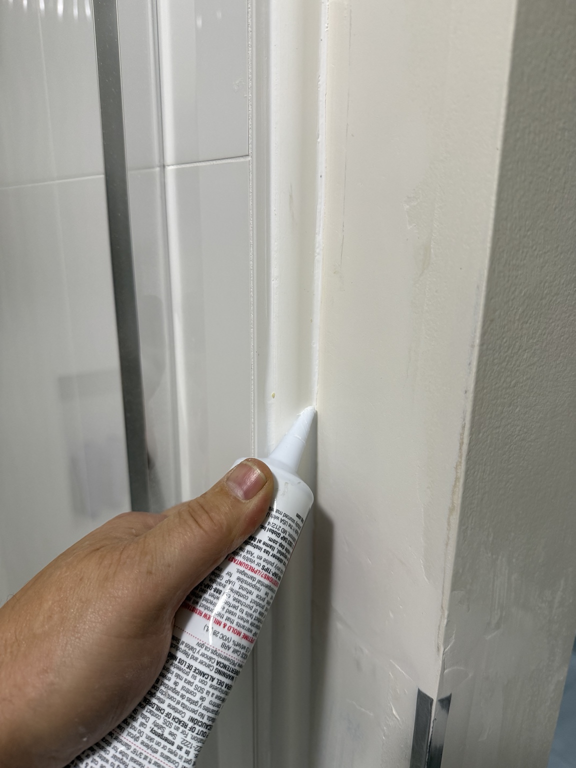 Applying compatible construction adhesive and caulk at the PVC shower trim